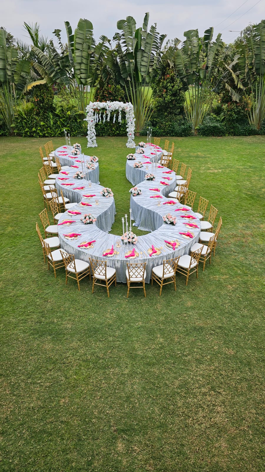 Curved banquet table dressed in silver with gold chiavari chairs and pink florals on the lawn