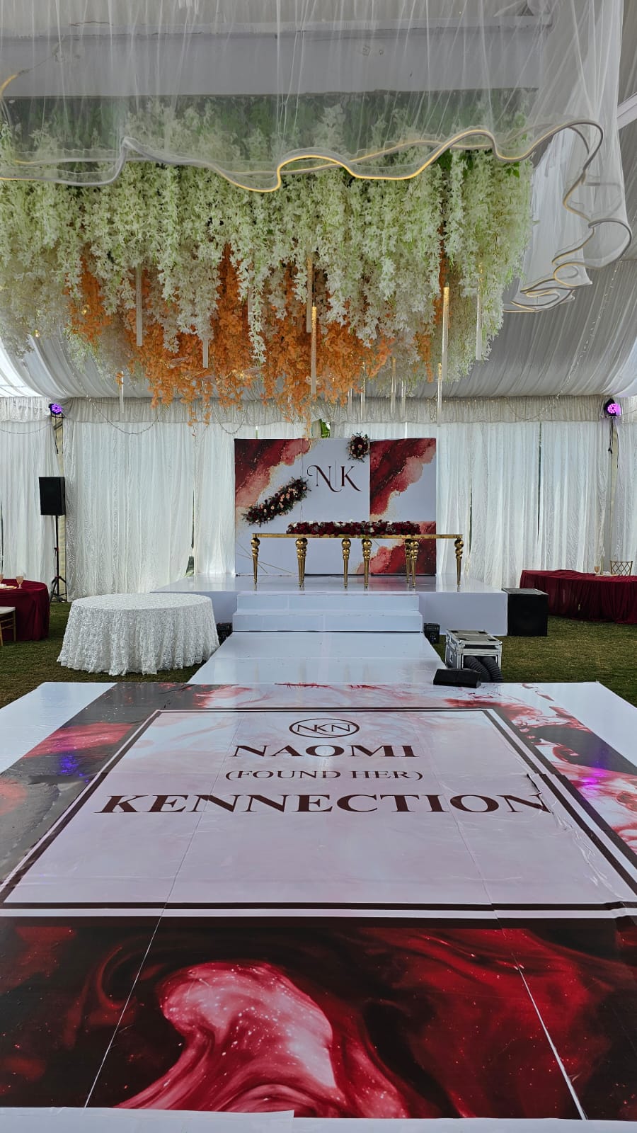 Marquee stage with a hanging floral ceiling, printed dance floor and decorated top table