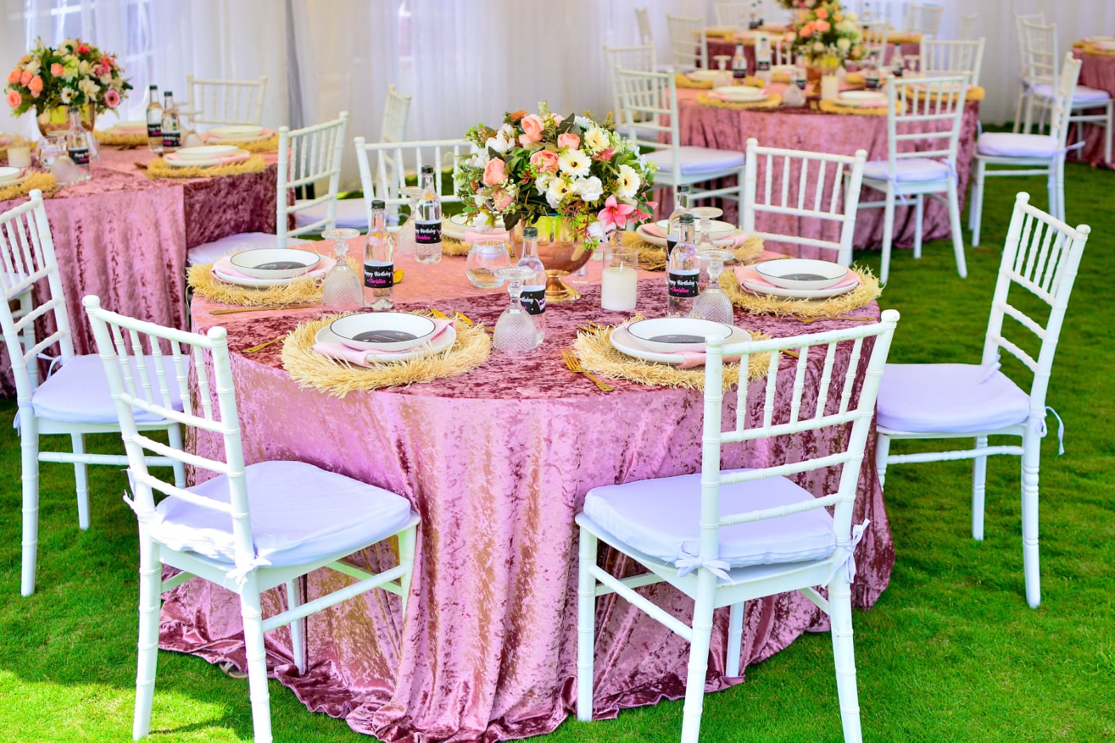 Dusty pink velvet round tables with white chiavari chairs and floral centrepieces inside a garden marquee