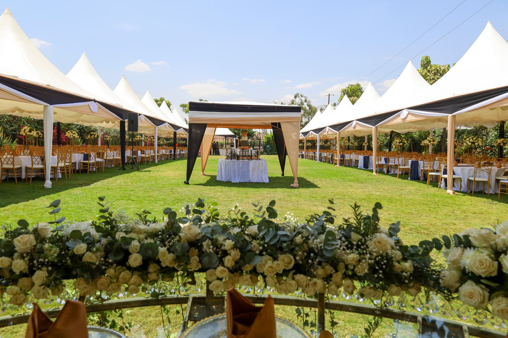 Sunlit garden reception with white canopies, gold chairs and floral table styling