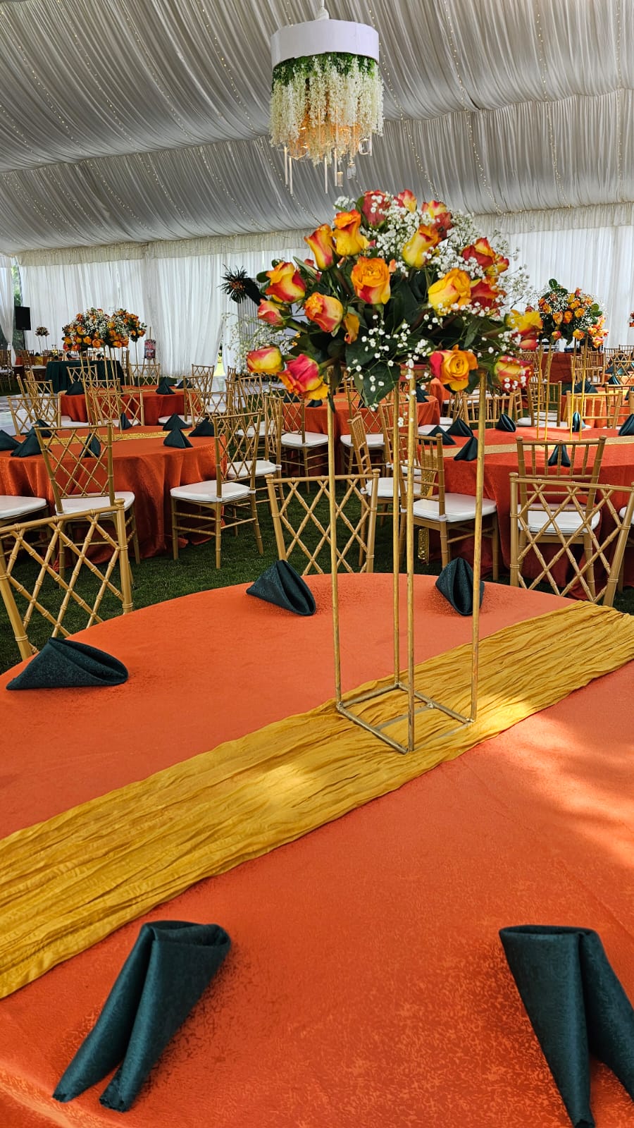 Marquee reception with orange linens, gold chiavari chairs, tall rose centrepieces and a floral chandelier