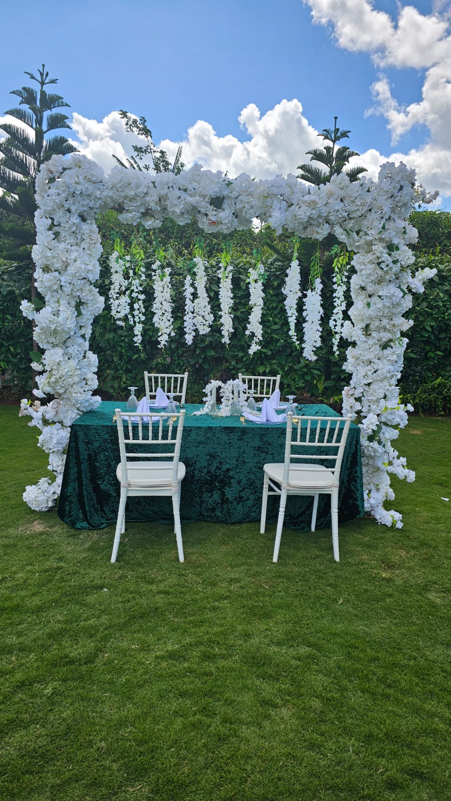 White floral arch over an emerald sweetheart table with white chiavari chairs on the lawn